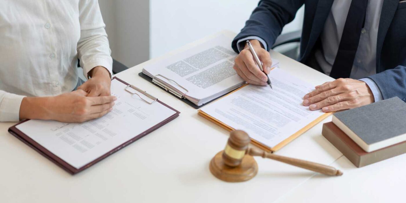 Lawyer and client reviewing and signing legal documents at a desk with a gavel and law books.